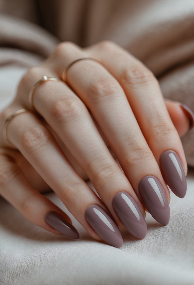 Close-up of a hand with almond-shaped nails painted dusty mauve resting on a neutral surface.