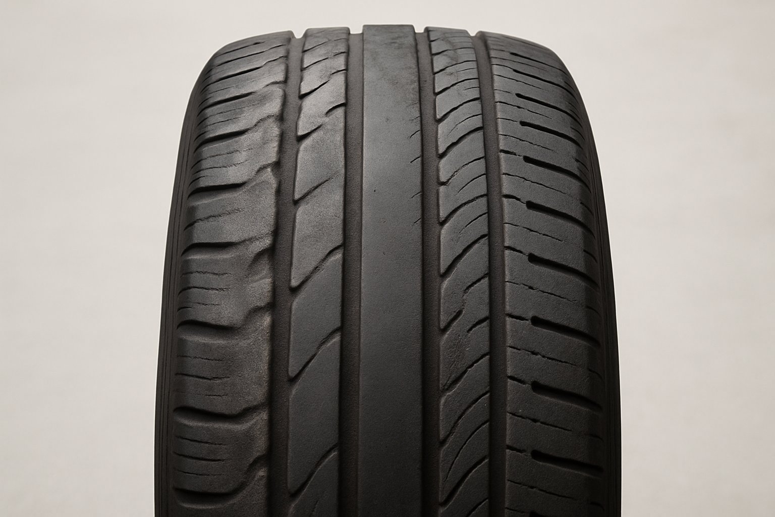Close-up of a car tire showing uneven tread wear patterns on a neutral background.