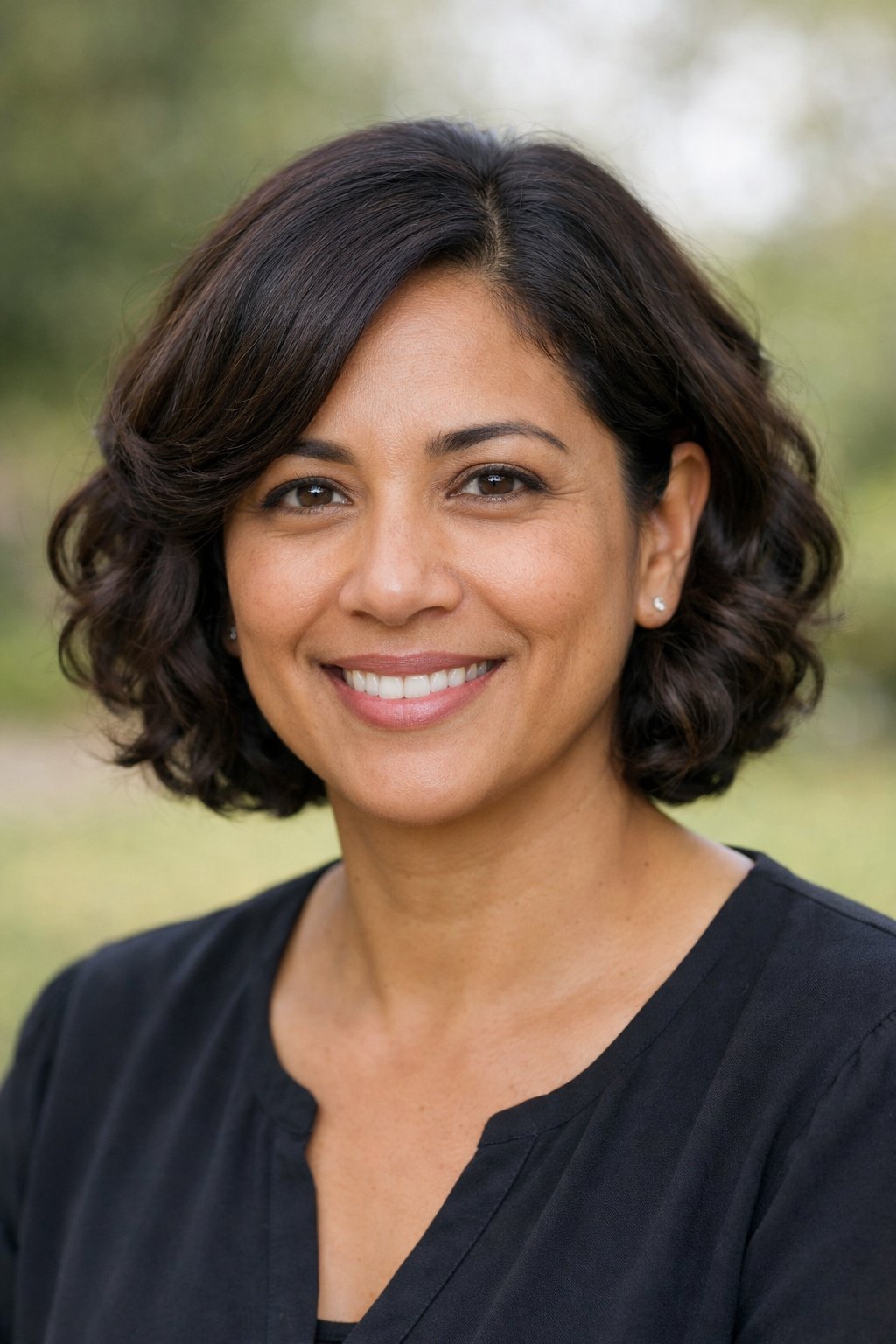Headshot of a smiling woman outdoors with a blurred natural background.