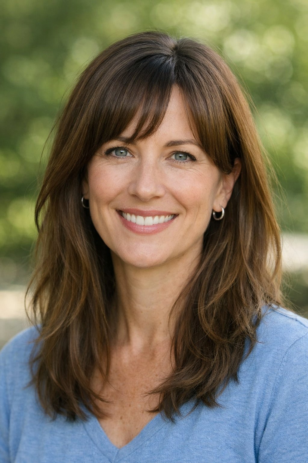 Headshot of a smiling woman outdoors with a side part and long curtain bangs hairstyle.