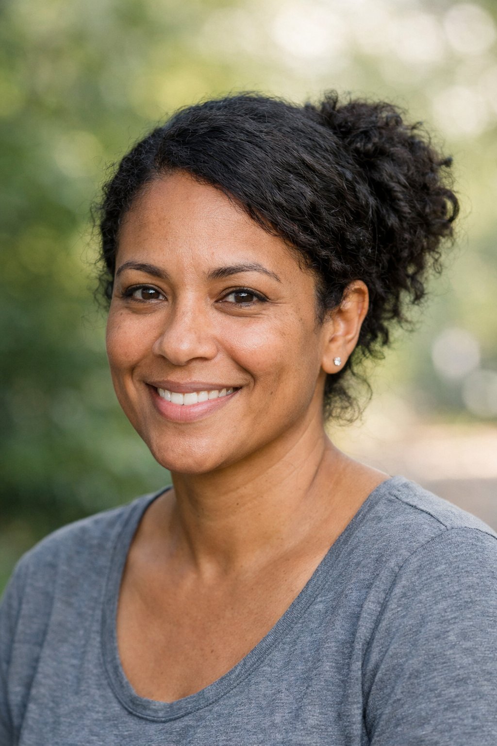 Headshot of a smiling woman outdoors with her hair styled in a side-part messy bun.