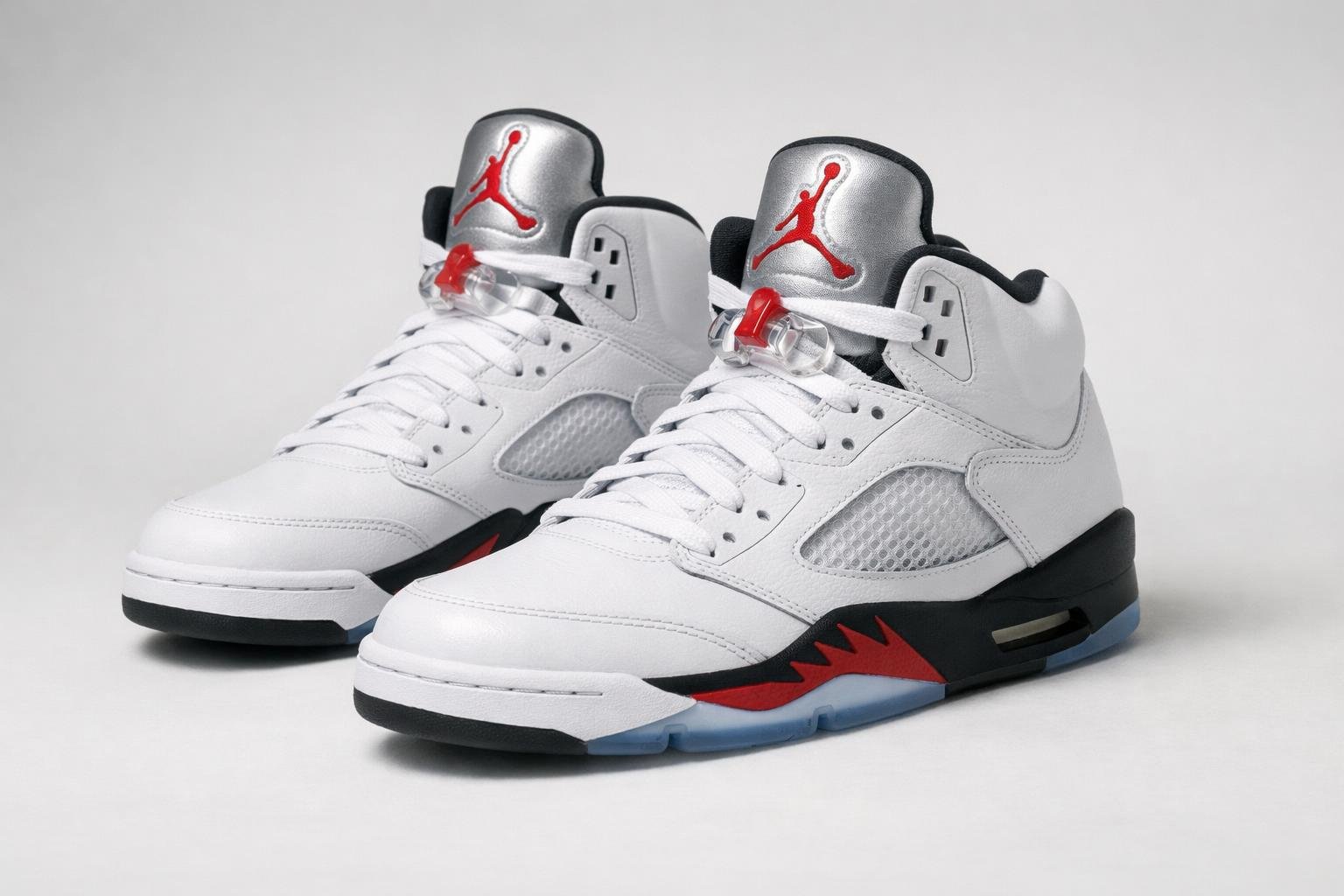 Sepasang sepatu Air Jordan 5 Retro diletakkan di atas latar belakang polos tanpa teks atau elemen lain.