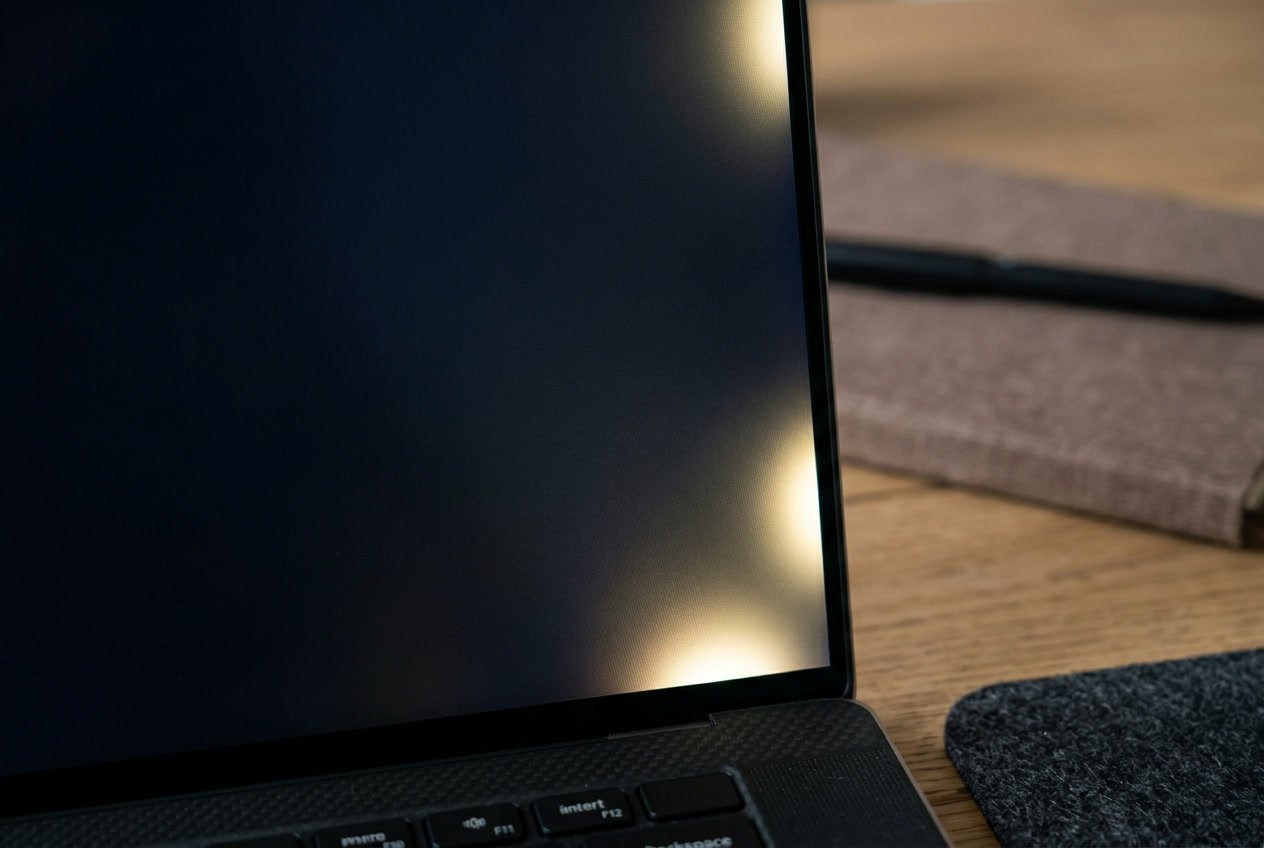 Close-up of a laptop screen showing light bleeding along the edges on a modern desk with a mouse and notebook nearby.