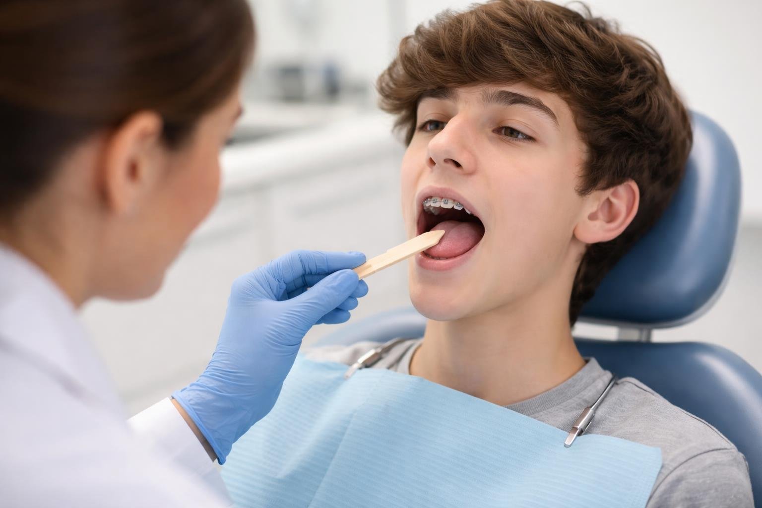 Un adolescente con brackets en una clínica ortodóntica, siendo examinado por un especialista que revisa la posición de la lengua.