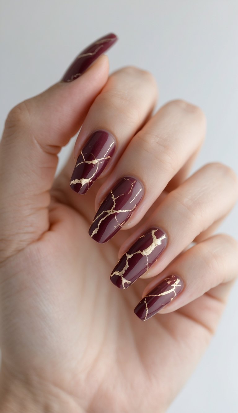 Close-up of one hand with burgundy marble nails featuring gold veining against a white background.