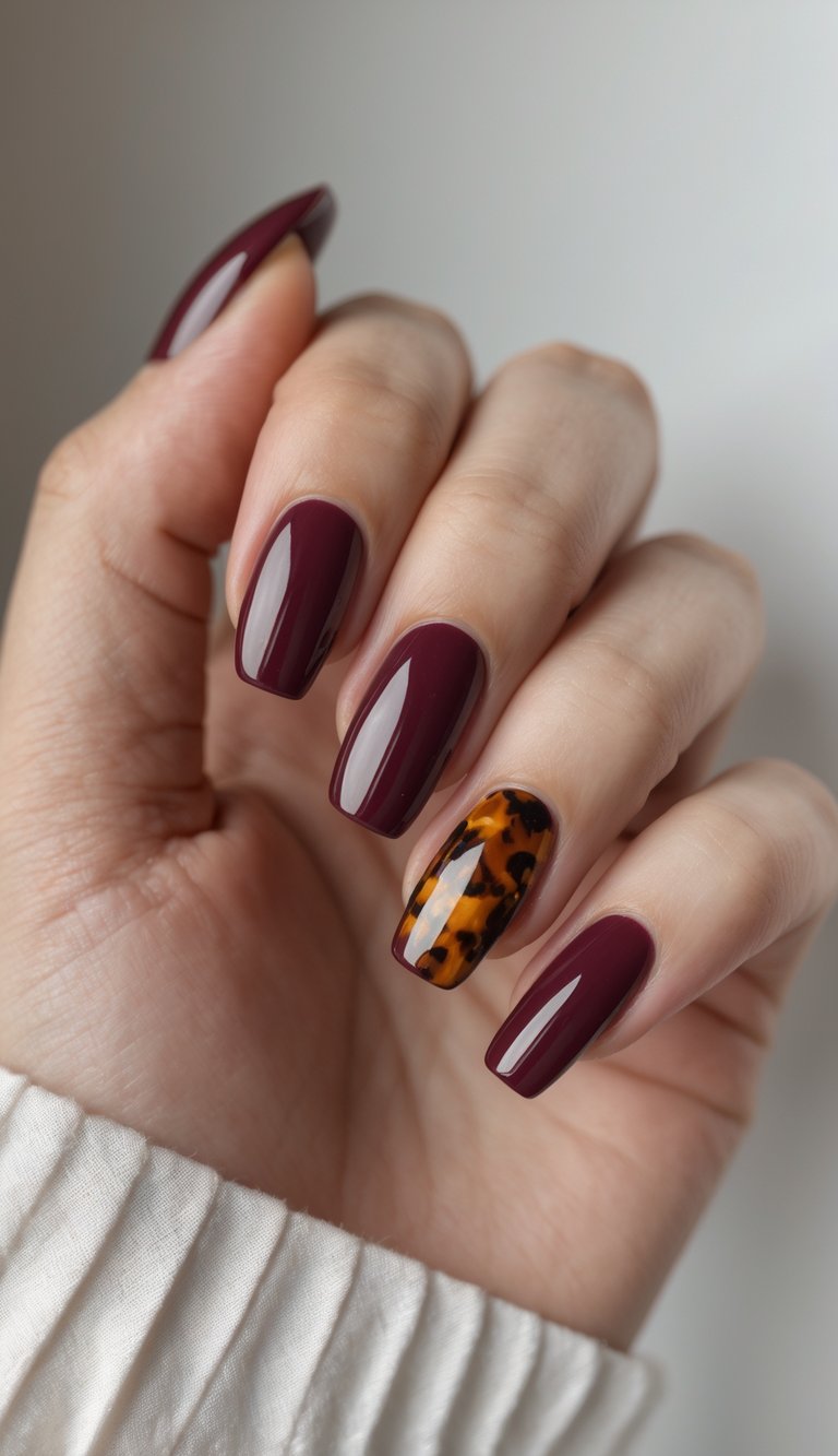 Close-up of one hand with burgundy and tortoiseshell patterned nails against a white background.