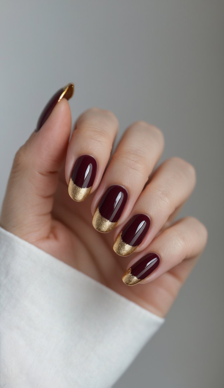 Close-up of one hand showing burgundy nails with gold tips against a white background.