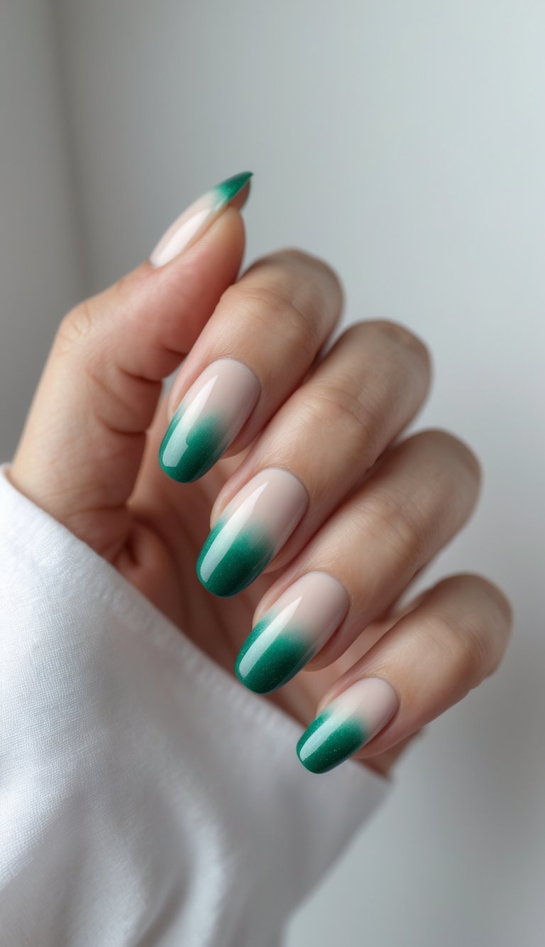 Close-up of one hand with nails painted in a gradient from milky nude to emerald green against a white background.