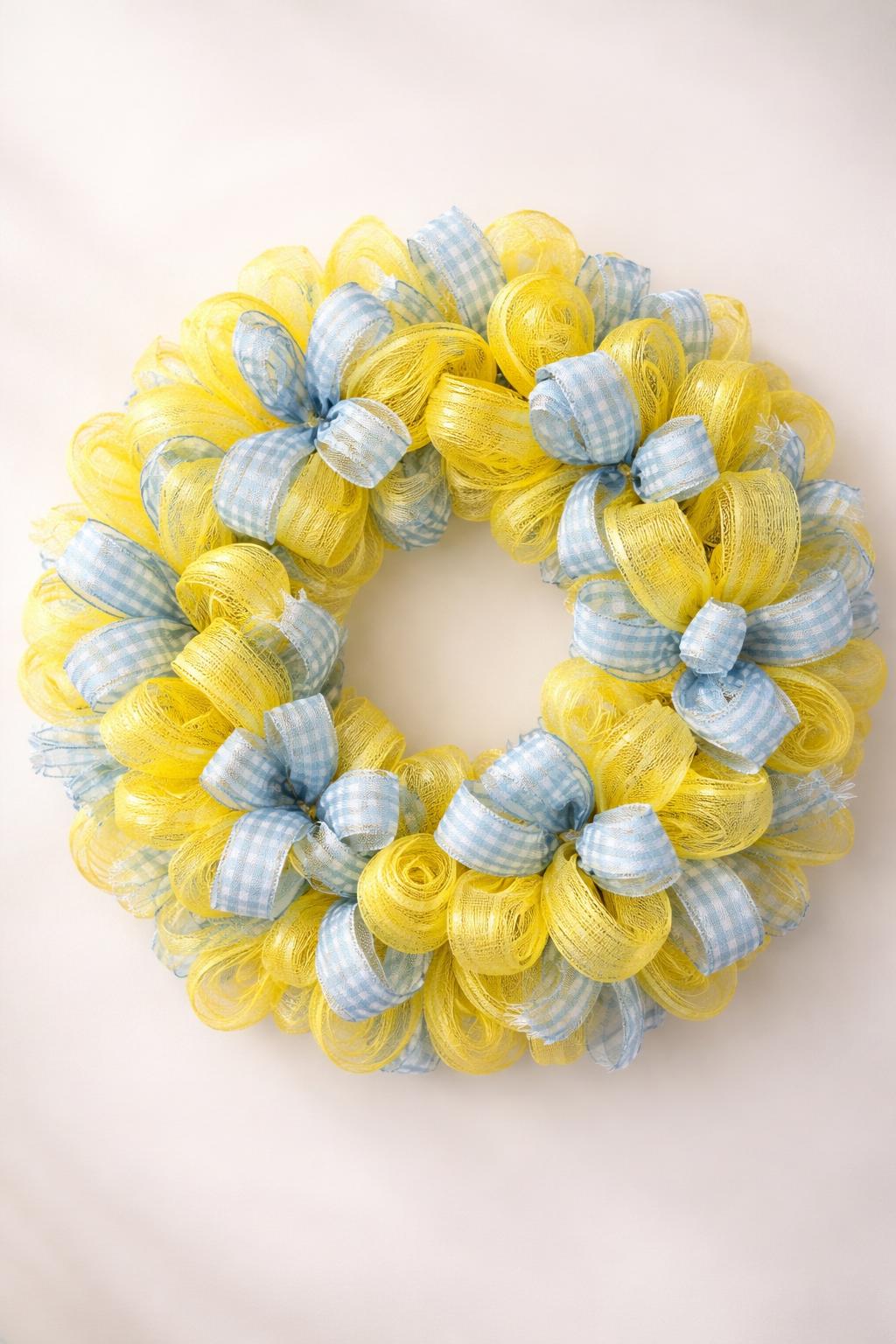 A circular wreath made of yellow and blue gingham mesh ribbons displayed against a plain background.