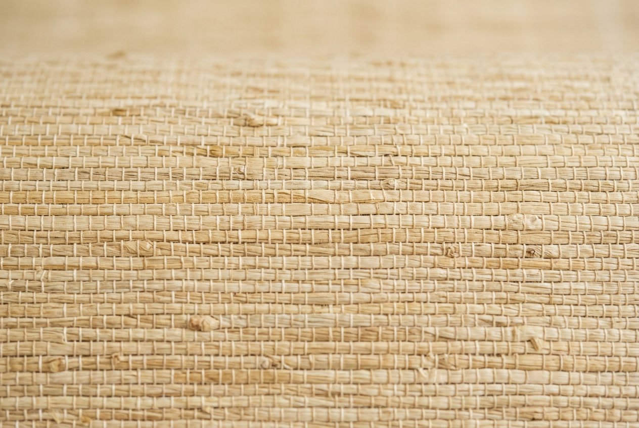 Close-up of textured warm beige grasscloth wallpaper showing natural woven fibers and visible horizontal seams.