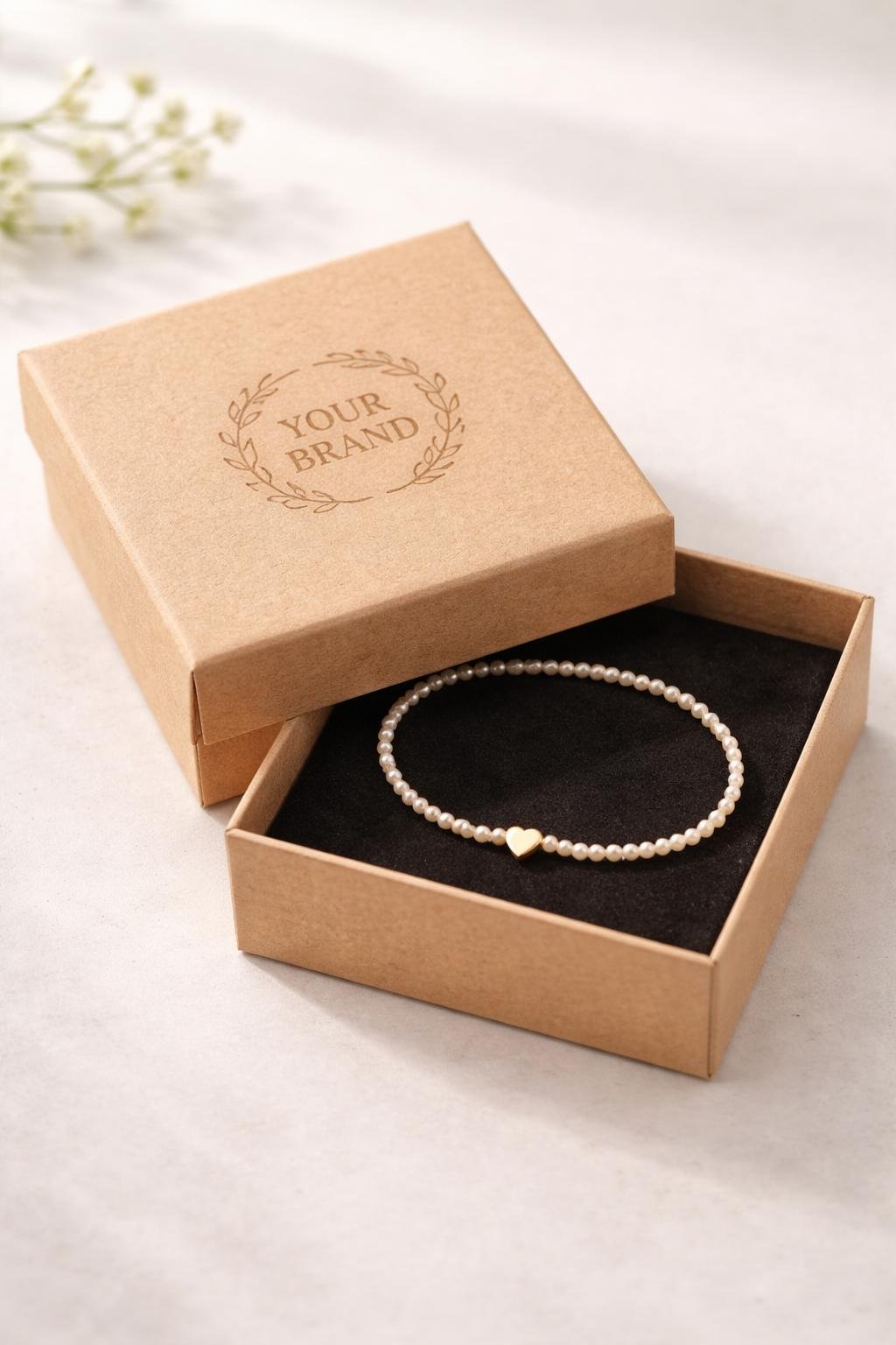 An open kraft paper jewelry box with a bracelet inside and a custom logo embossed on the lid.