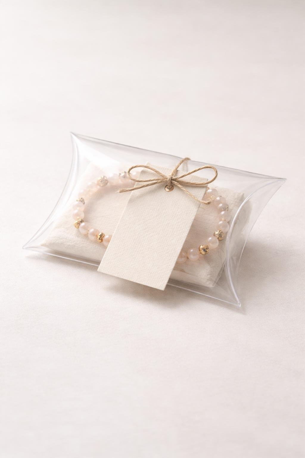 A clear pillow box with a printed thank-you tag attached, containing small items, placed on a neutral background.