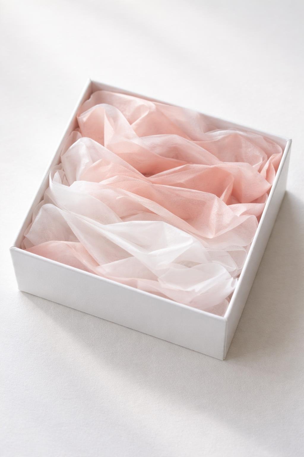Jewelry gift box filled with layered blush pink and white tissue paper arranged in soft folds.