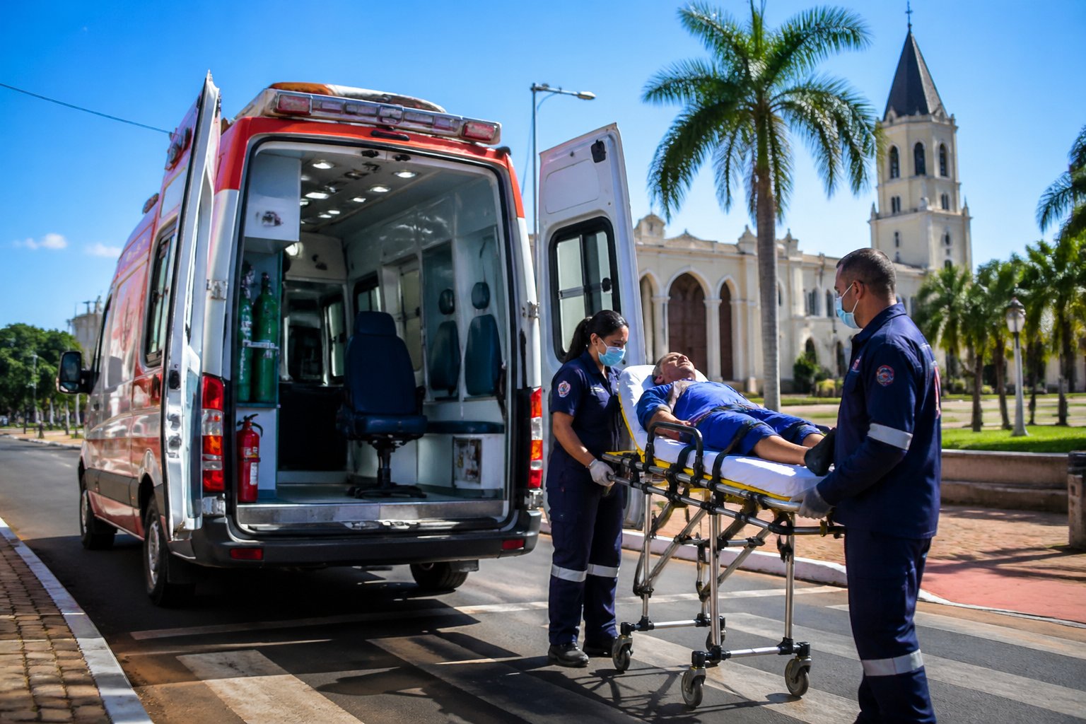 Ambulância estacionada em uma rua urbana de Alto Paraná com paramédicos atendendo um paciente em uma maca.