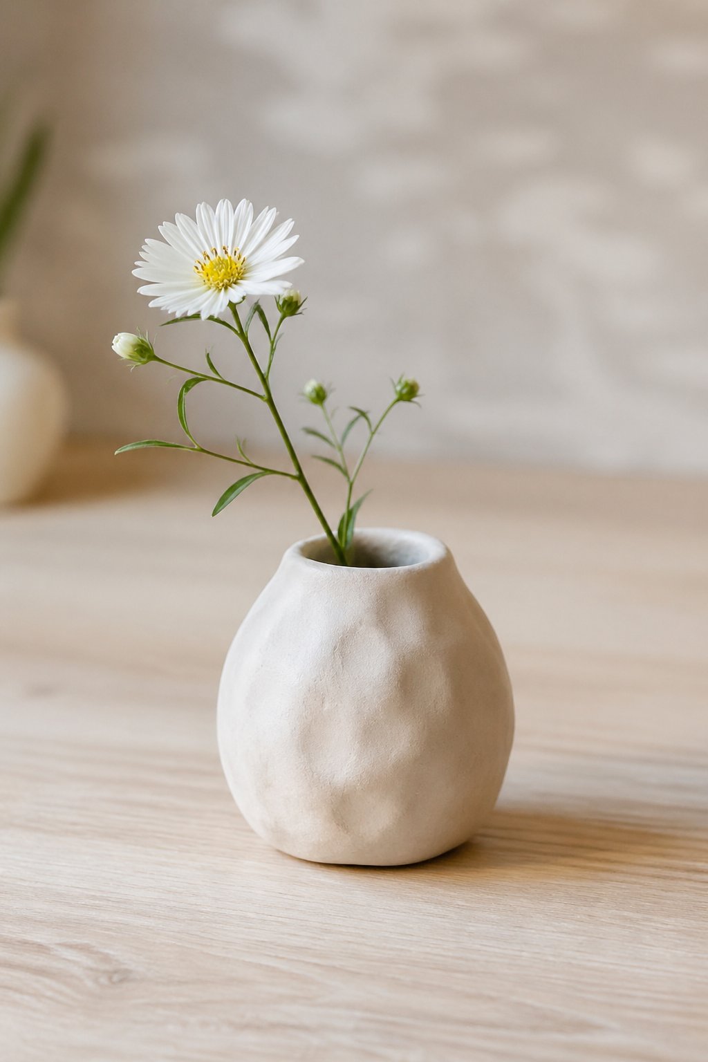A small handmade clay bud vase holding a single delicate flower on a wooden surface.