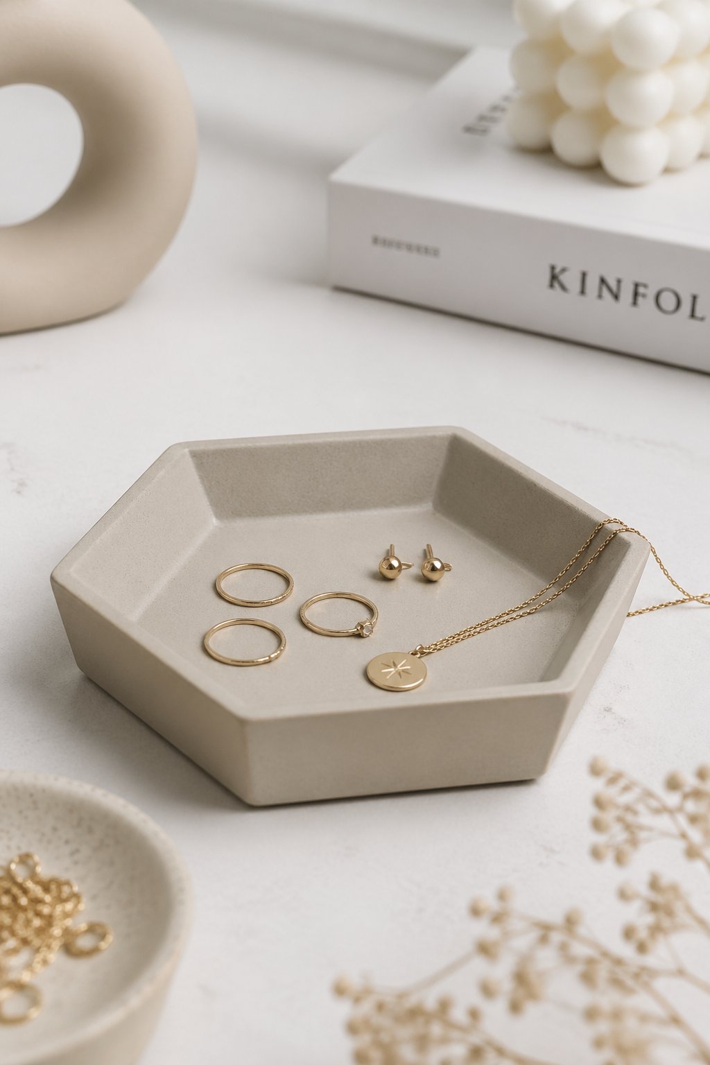 A clay geometric catchall dish holding small jewelry pieces and trinkets on a light surface.