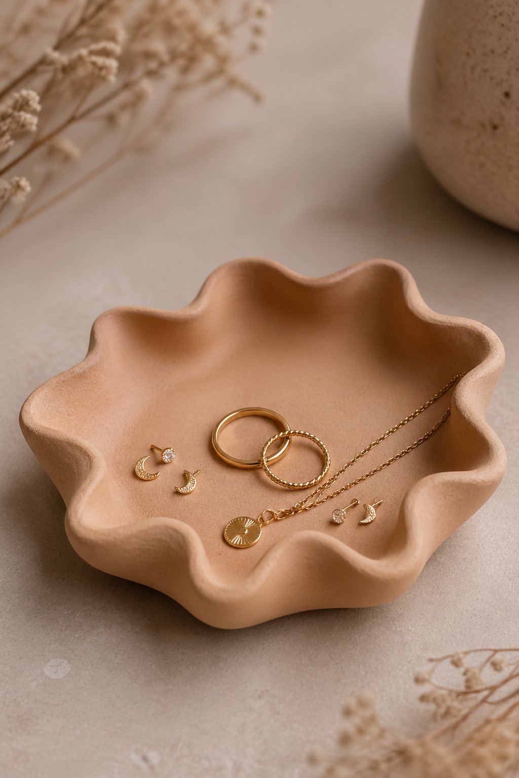 A wavy-edge clay dish holding small jewelry pieces like rings and earrings on a neutral surface.
