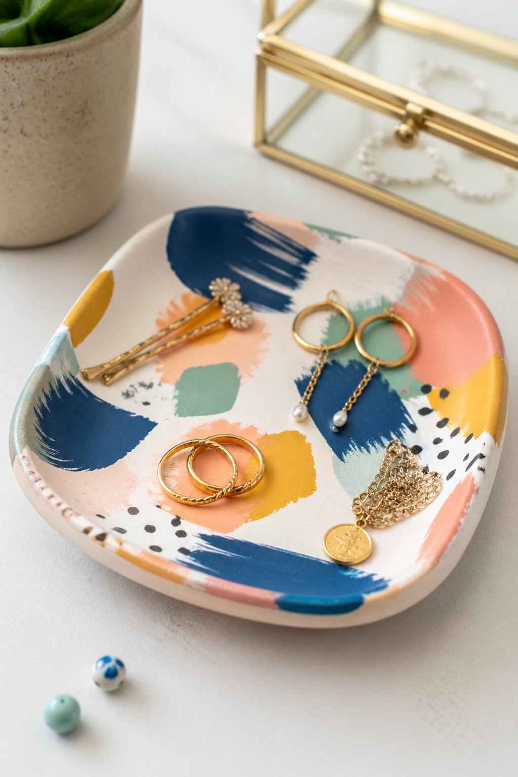 A clay trinket tray with colorful abstract patterns holding small jewelry and accessories on a clean surface.