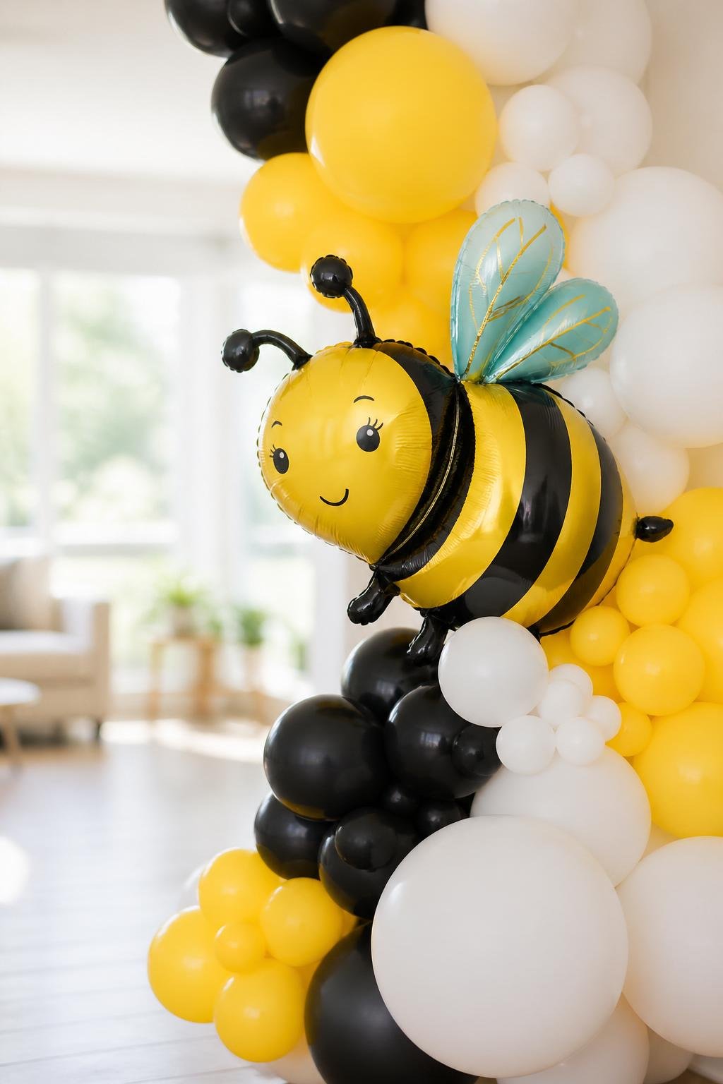A colorful balloon garland in yellow, white, and black with a large bee-shaped foil balloon.