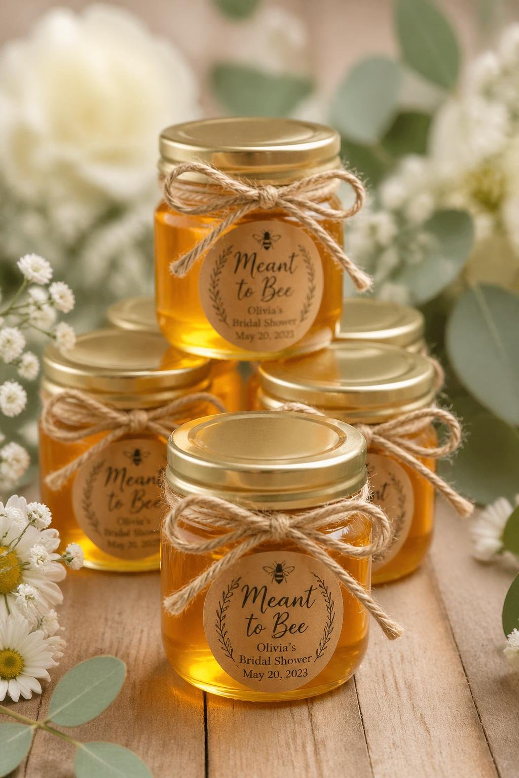 Mini mason jars filled with honey and tied with ribbons arranged on a wooden surface with soft floral background.