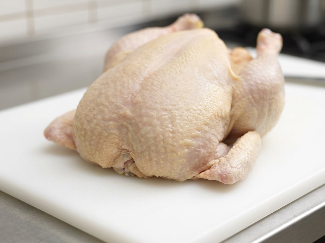 Raw whole chicken on a cutting board showing the breast section prominently.