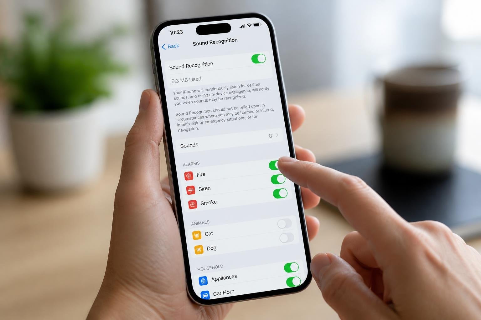 Close-up of a person holding an iPhone showing sound recognition settings on the screen.