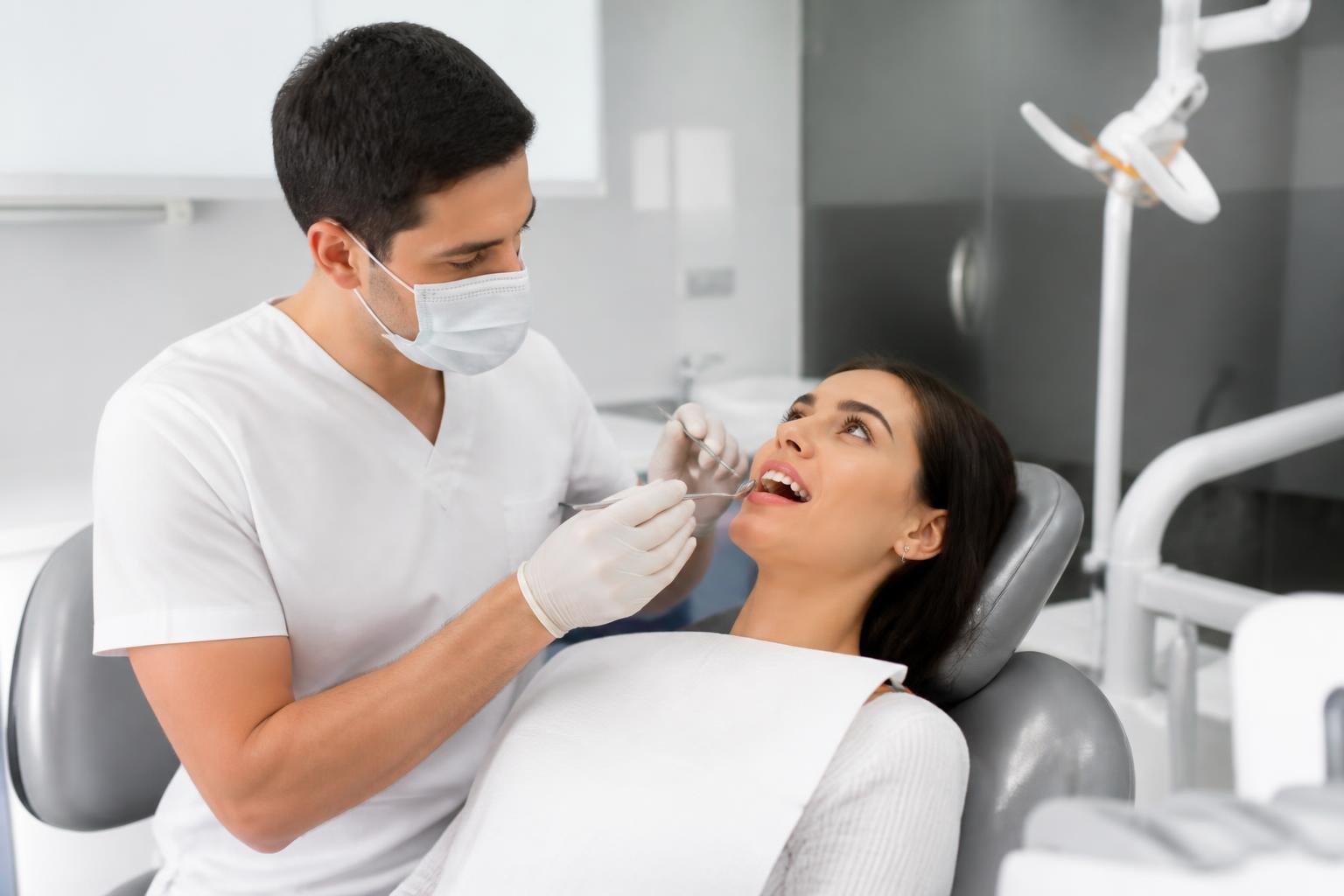 Dentist examining a patient's teeth in a modern dental clinic, with dental equipment visible in the background.