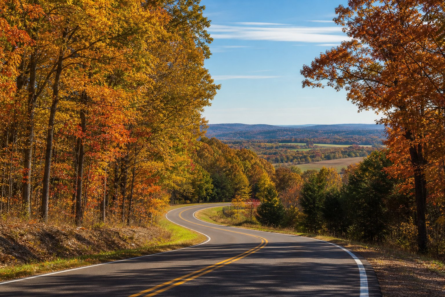 A winding country road surrounded by colorful autumn trees in Lafayette County near Oxford, Mississippi, with rolling hills and a clear sky in the background.
