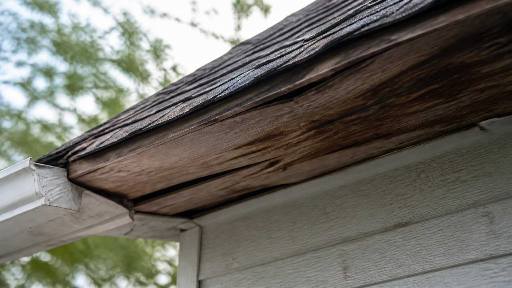 Close-up view of a sagging roof deck near the eaves of a house showing bowed wooden boards under the roof overhang.