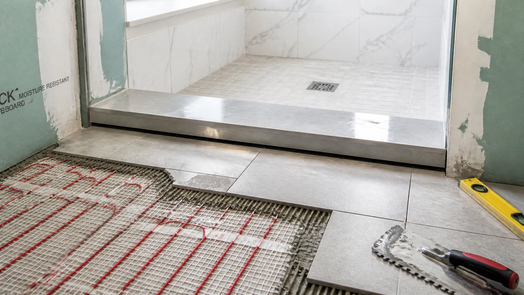 Close-up of heated tile floor installation beneath a new shower threshold in a bathroom under renovation.