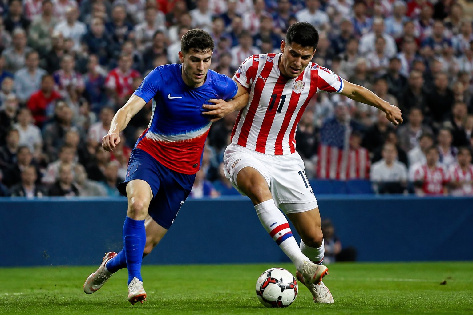 ABD ve Paraguay takımlarının futbol maçında top için mücadele eden oyuncular ve kalabalık stadyum.