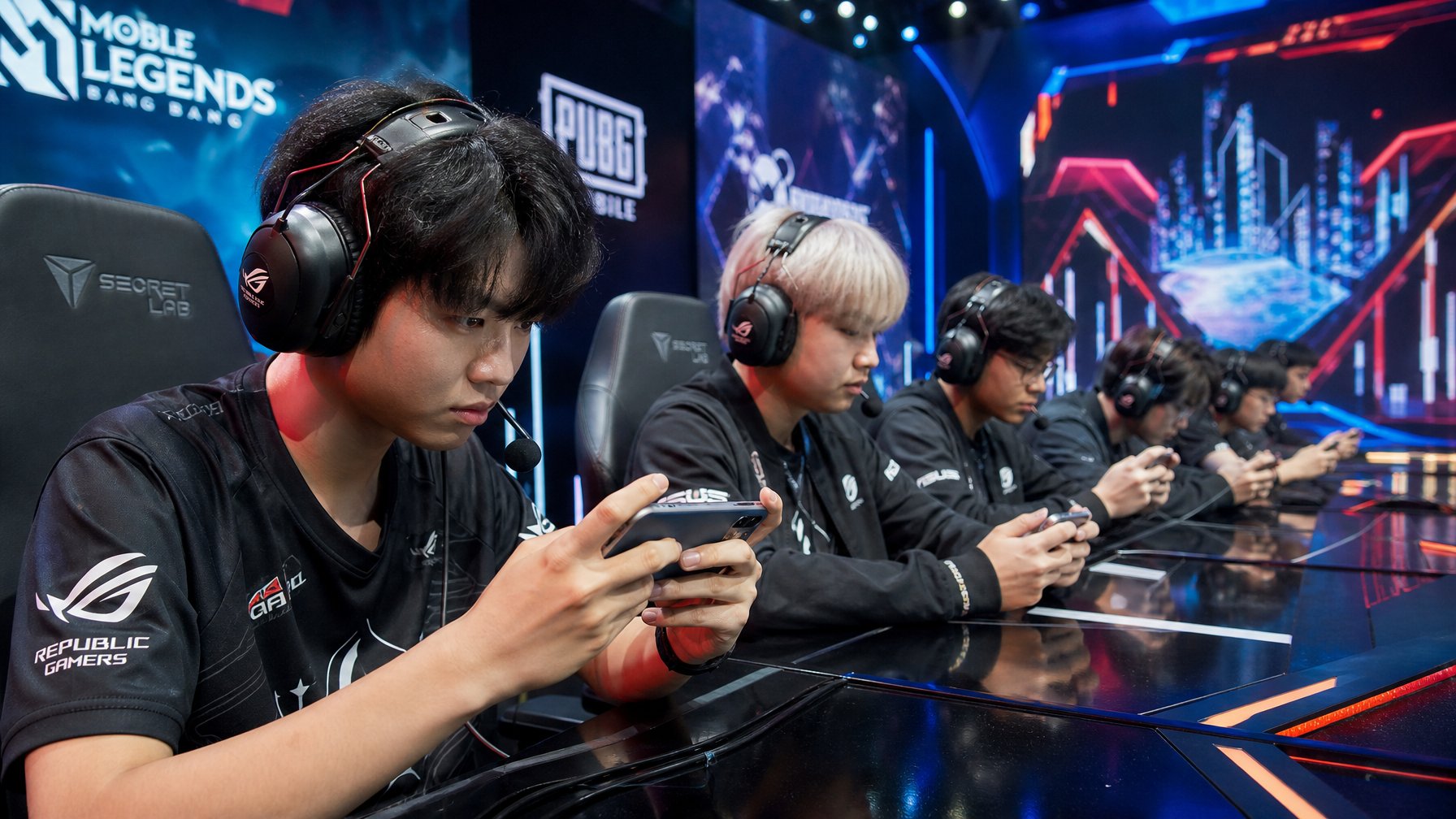 Sekelompok pemain muda sedang bermain game esports mobile dengan serius di ruangan gaming modern yang dilengkapi lampu LED dan layar digital.