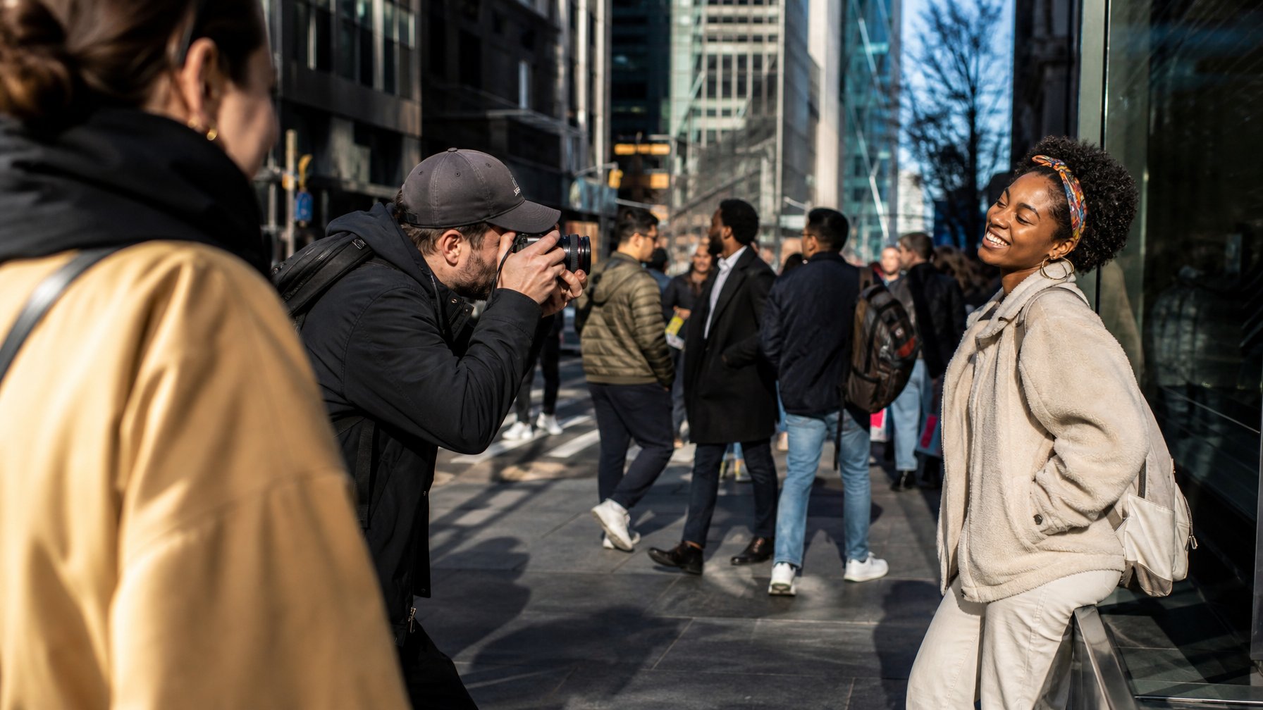 Seorang fotografer jalanan sedang mengambil gambar momen spontan di jalan kota yang ramai dengan orang-orang beraktivitas.