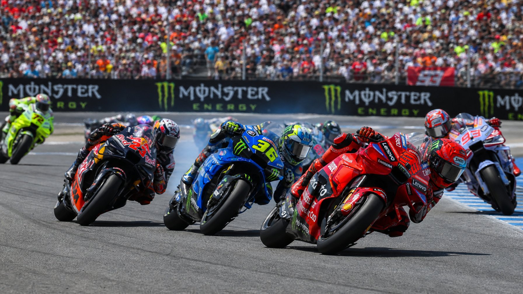Beberapa pembalap MotoGP sedang berlomba ketat di lintasan balap dengan penonton di tribun belakang.