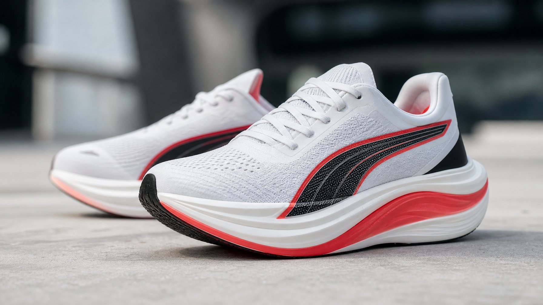 Sepasang sepatu lari Puma terbaru warna putih dengan aksen merah dan hitam, diletakkan di permukaan bersih dengan latar belakang kabur.