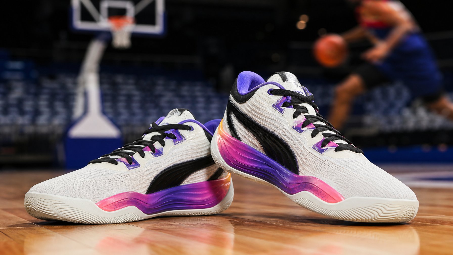 Sepasang sepatu basket Puma All-Pro NITRO 2 2026 diletakkan di lantai lapangan basket dengan latar belakang ring basket yang samar.