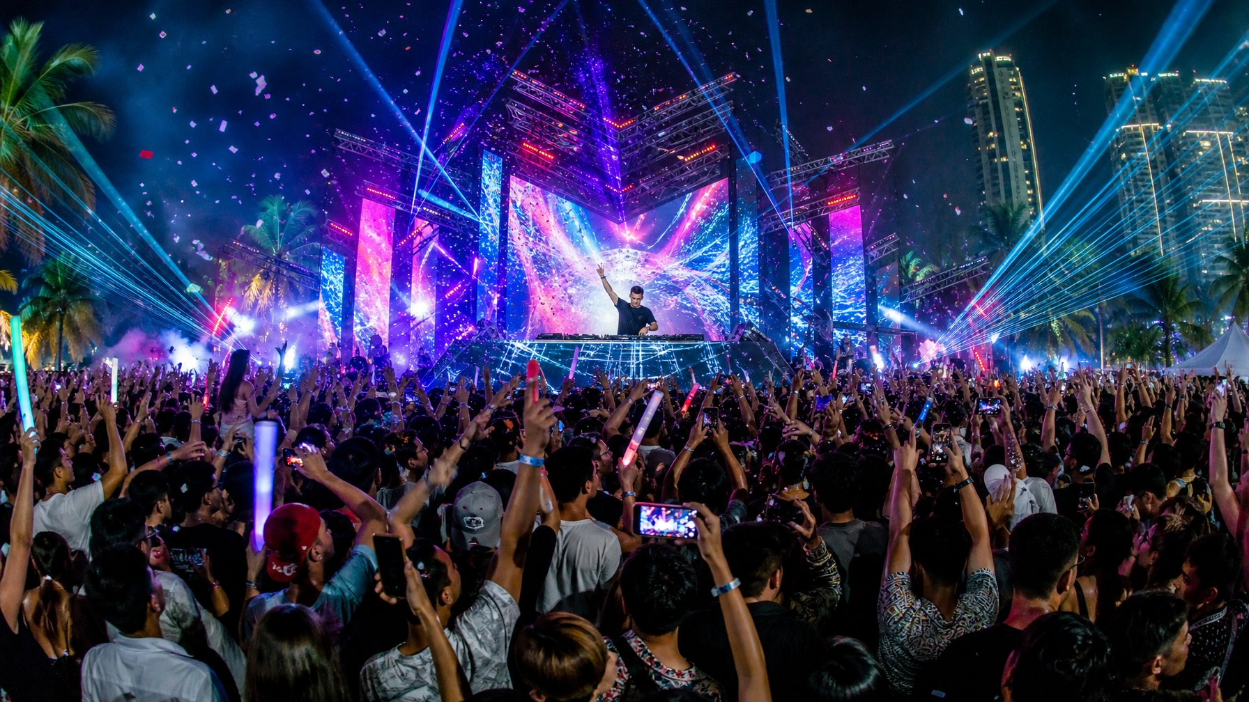 Kerumunan orang muda menari dan menikmati pesta malam EDM di luar ruangan dengan DJ internasional tampil di panggung, lampu warna-warni dan efek cahaya menghiasi suasana malam.