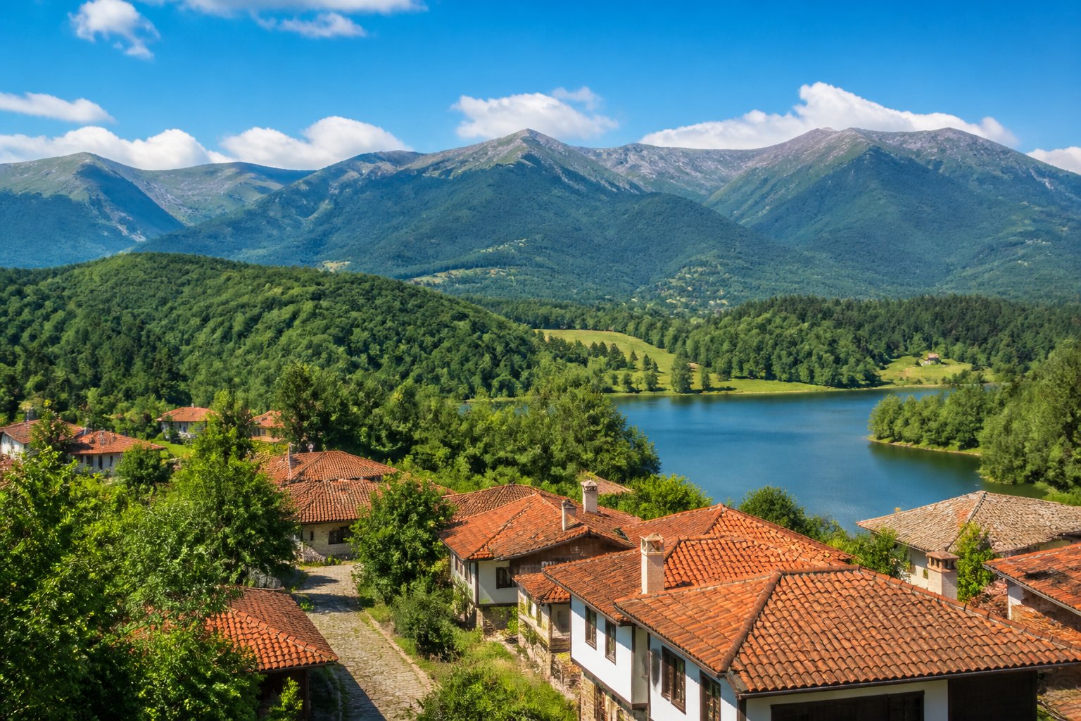 A scenic view of the Balkan Mountains in Bulgaria with green forests, traditional houses, and a clear sky.