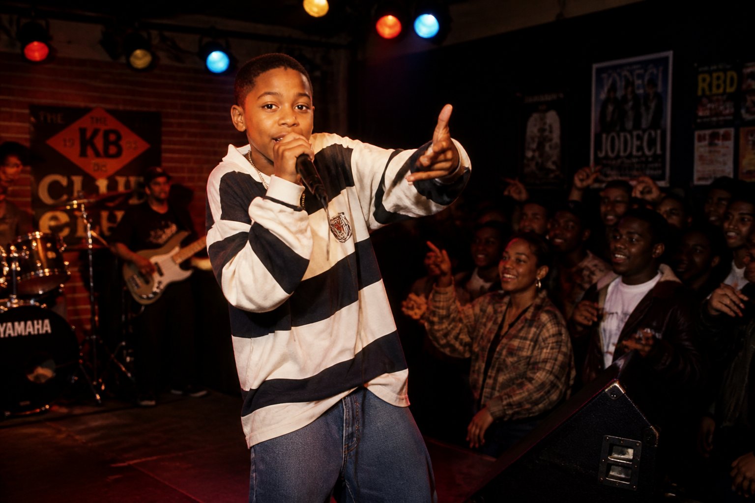 A young boy singing on stage in a lively club with a small audience watching.