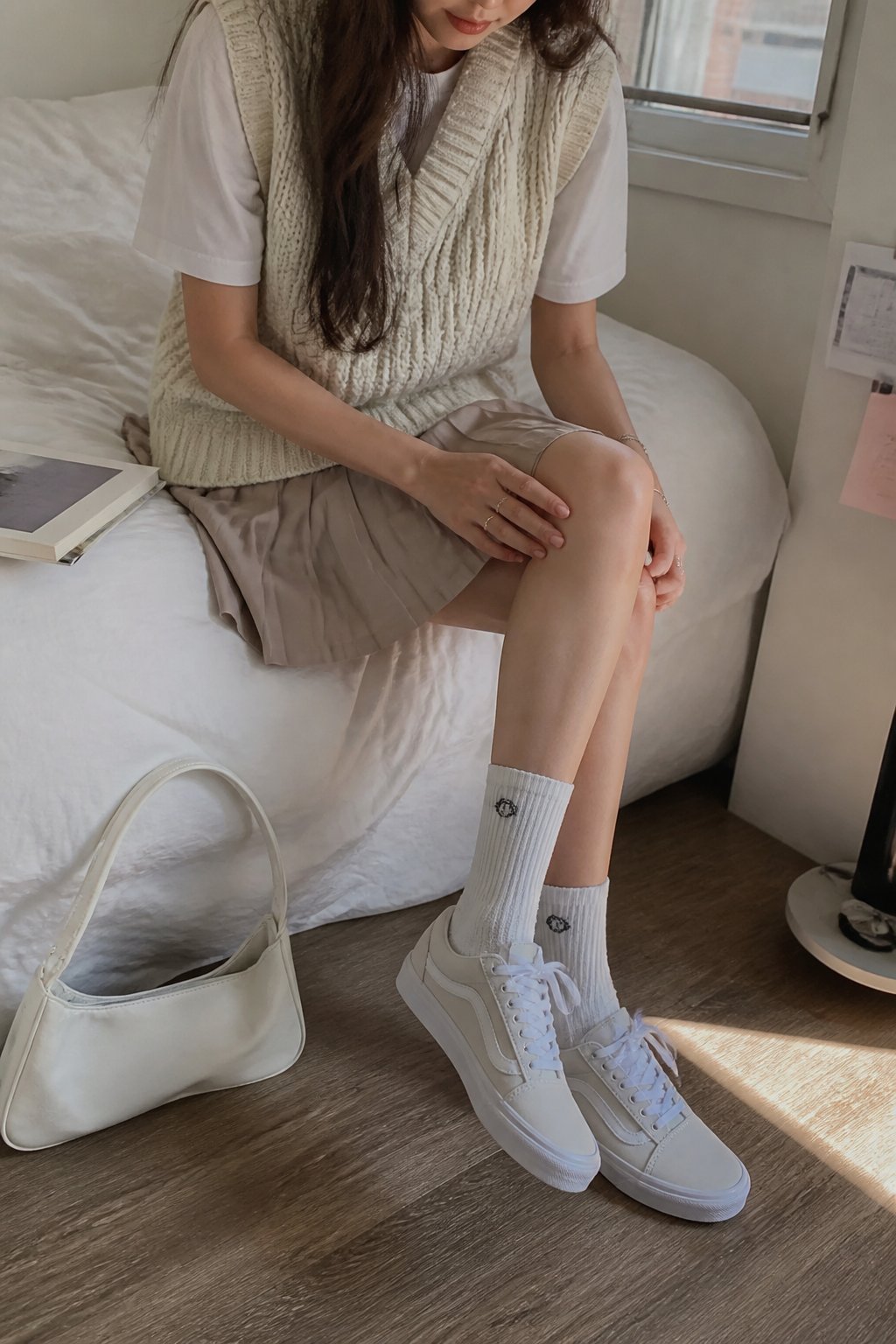 A person wearing pearlized Vans Old Skool 36 sneakers with a pleated skirt, crew socks, and a knit vest, standing casually in soft daylight with natural shadows and a slightly off-center composition.