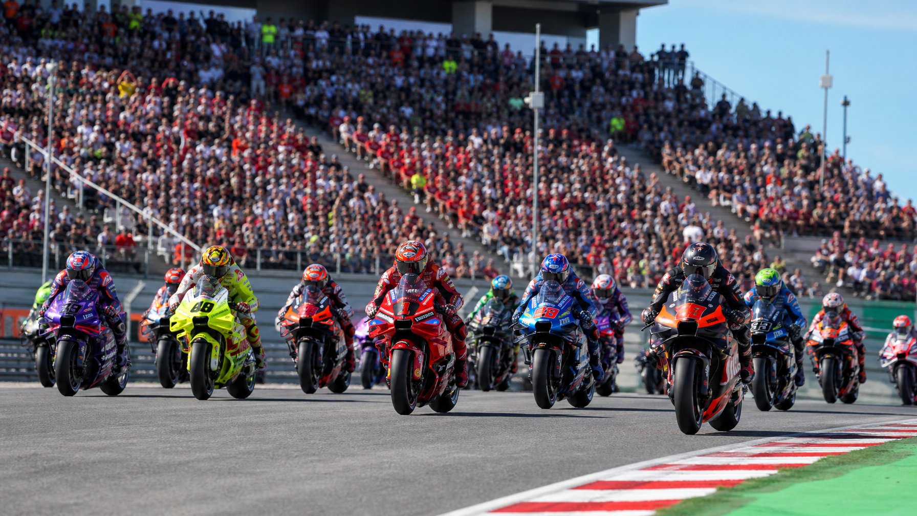 Sejumlah pembalap MotoGP dengan motor balap mereka sedang bersiap di lintasan balap dengan penonton di tribun stadion.