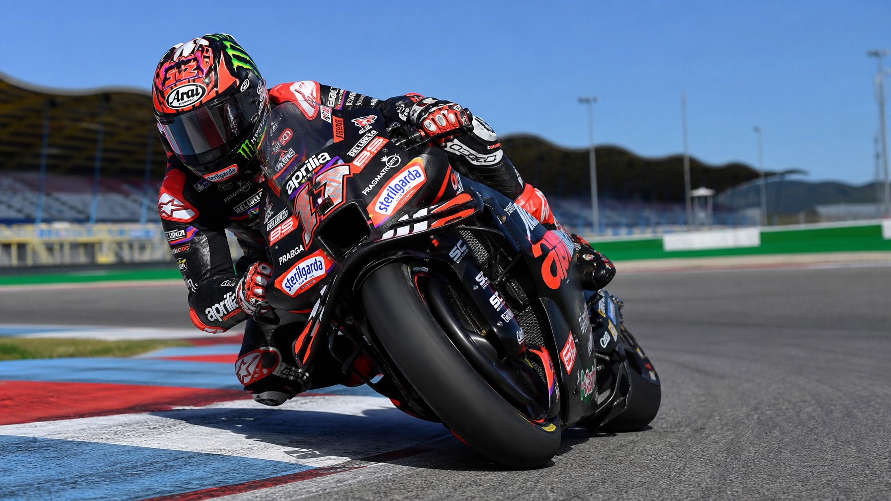 Seorang pembalap MotoGP sedang membelok tajam di lintasan balap dengan motor balap modern dan perlengkapan lengkap.