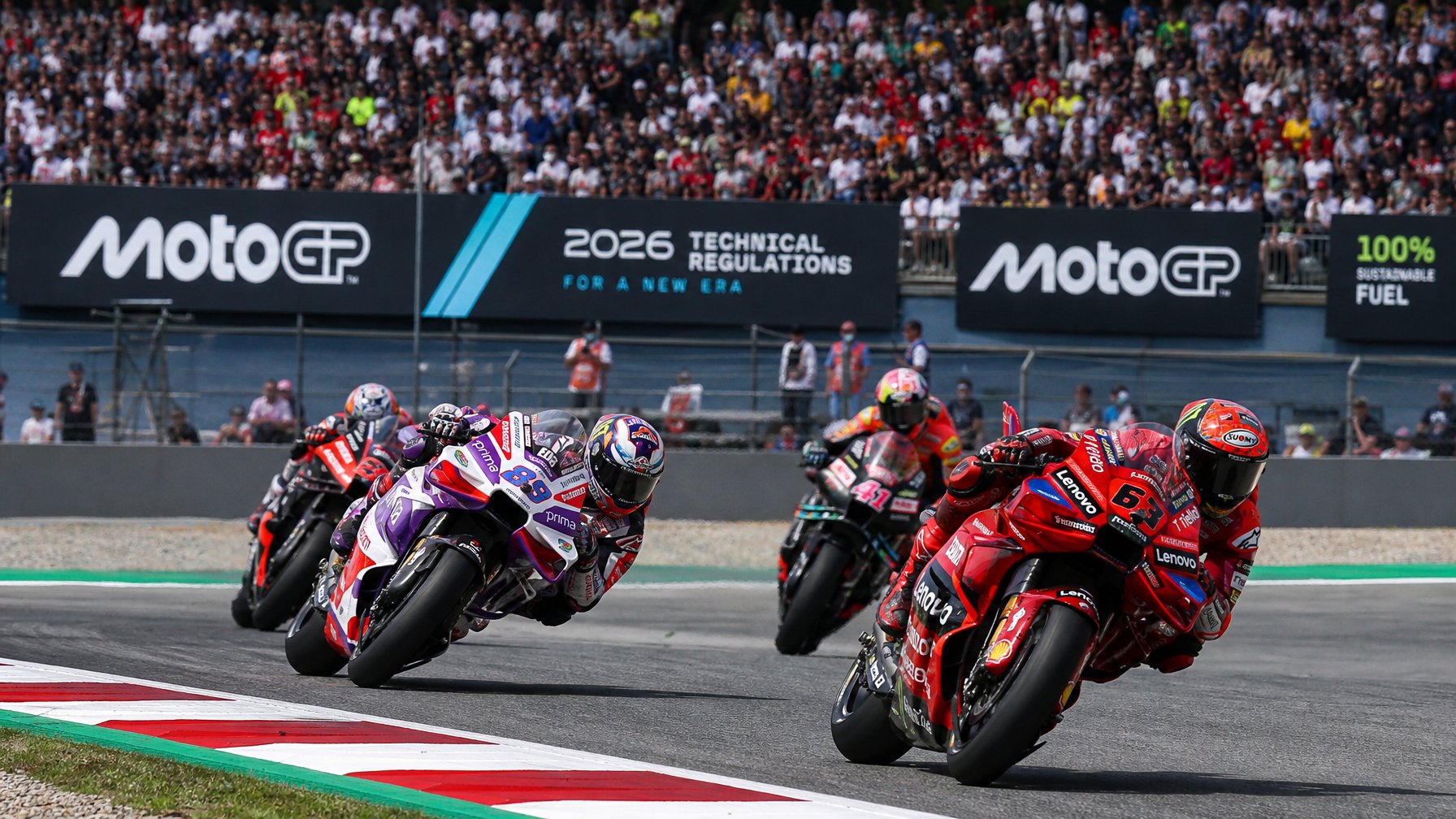 Pembalap MotoGP sedang berlomba di lintasan balap dengan motor futuristik dan penonton di tribun.