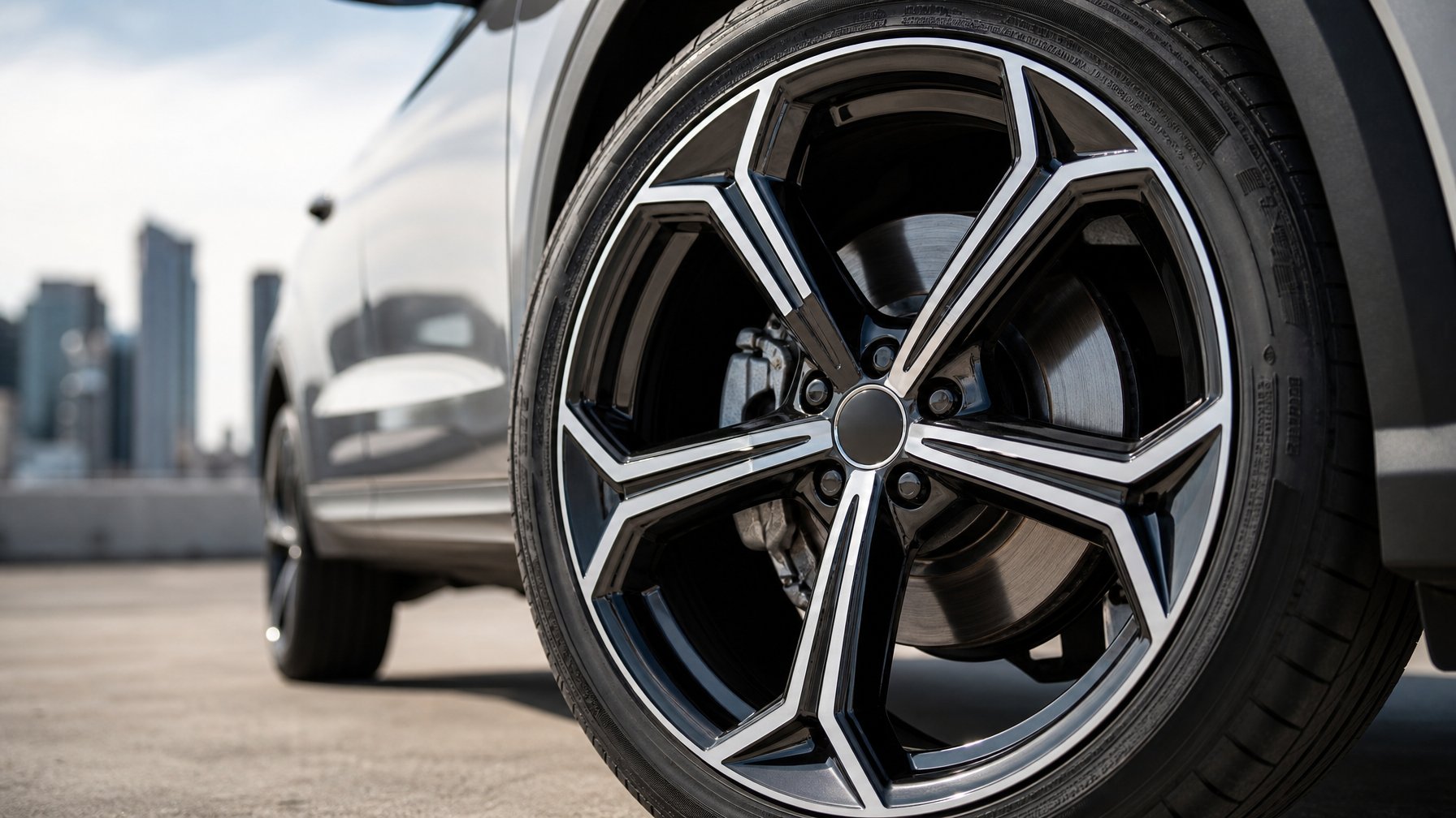 Gambar close-up velg mobil modern dengan desain elegan dan latar belakang kota samar.