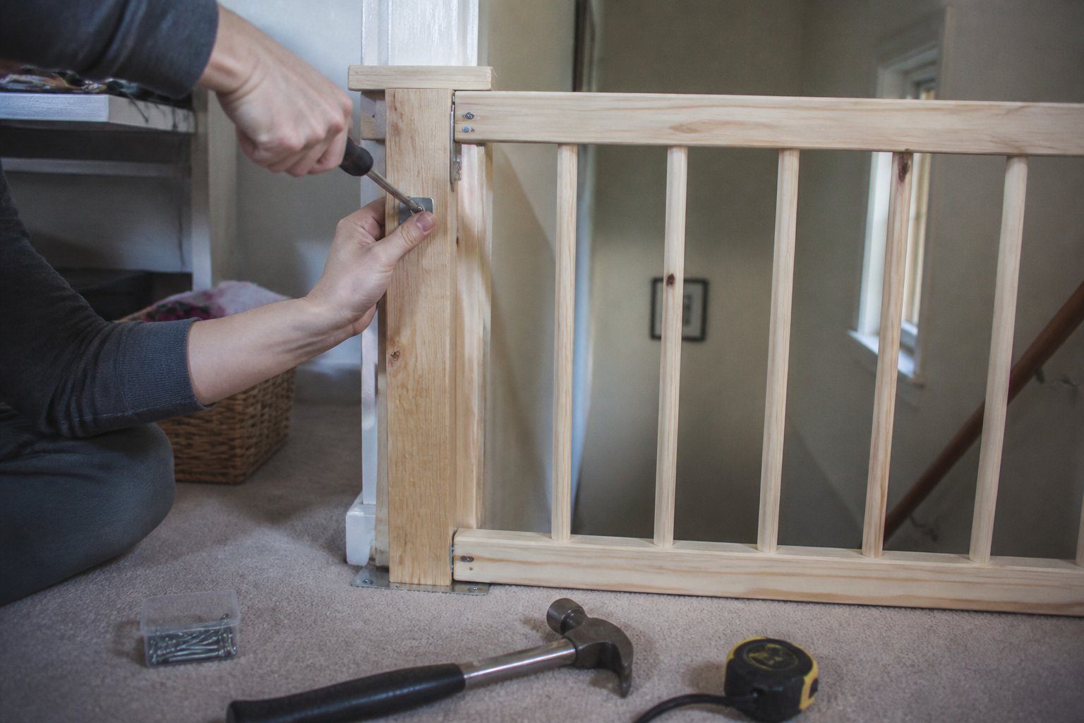 Hands assembling a simple wooden stairway gate on a home staircase with tools nearby.
