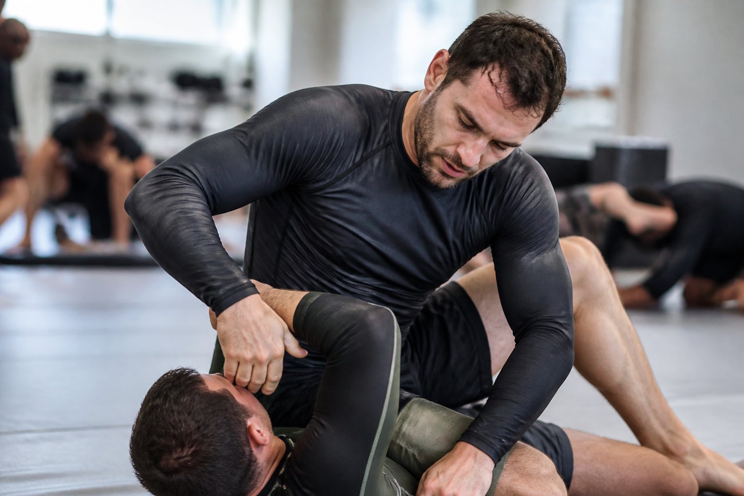 A person practicing Brazilian Jiu-Jitsu wearing a durable rash guard while training on a gym mat.