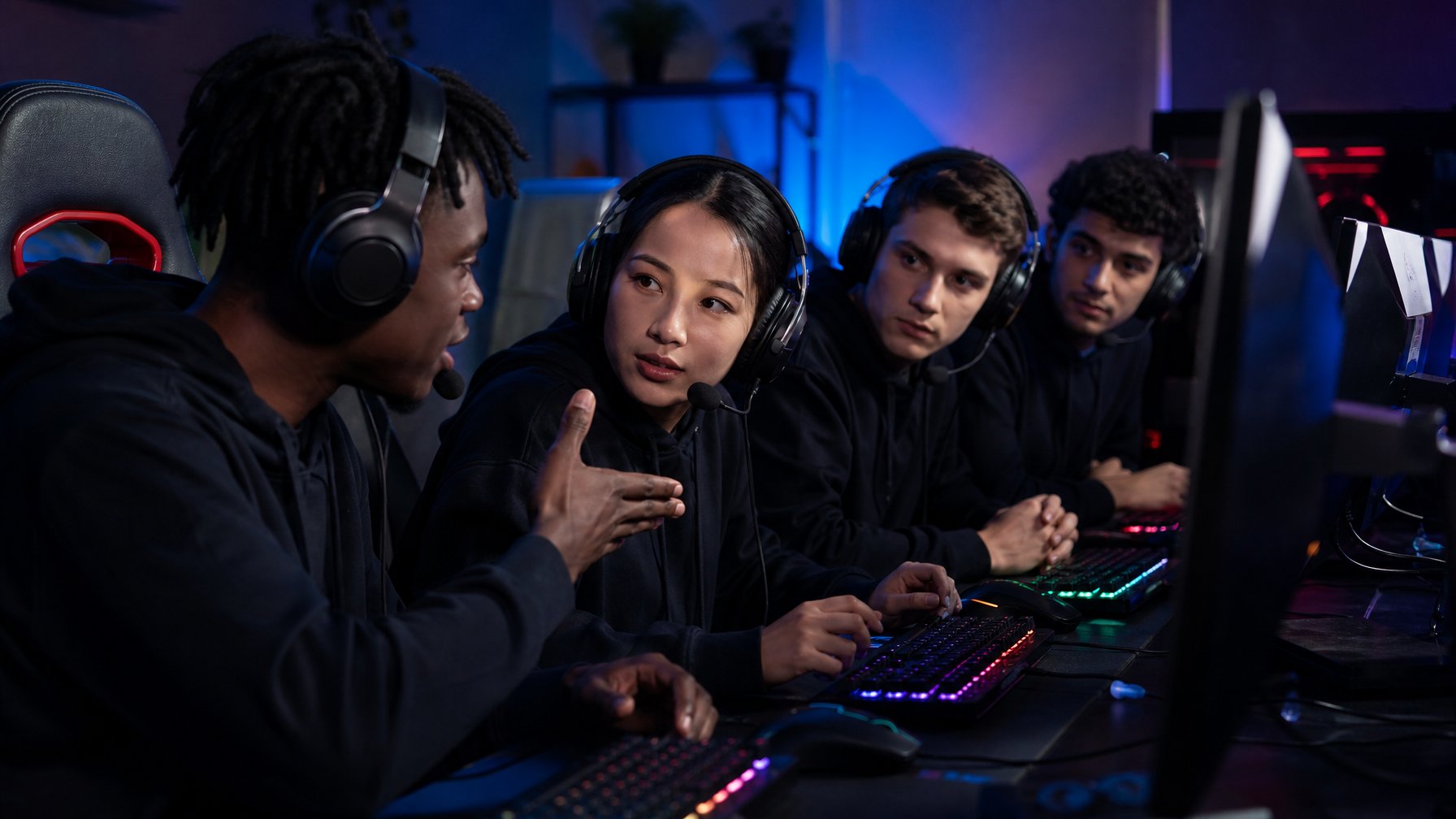 Sekelompok orang muda sedang bermain game tim Counter-Strike 2 dengan serius dan berkomunikasi menggunakan headset di ruang gaming berlampu warna-warni.