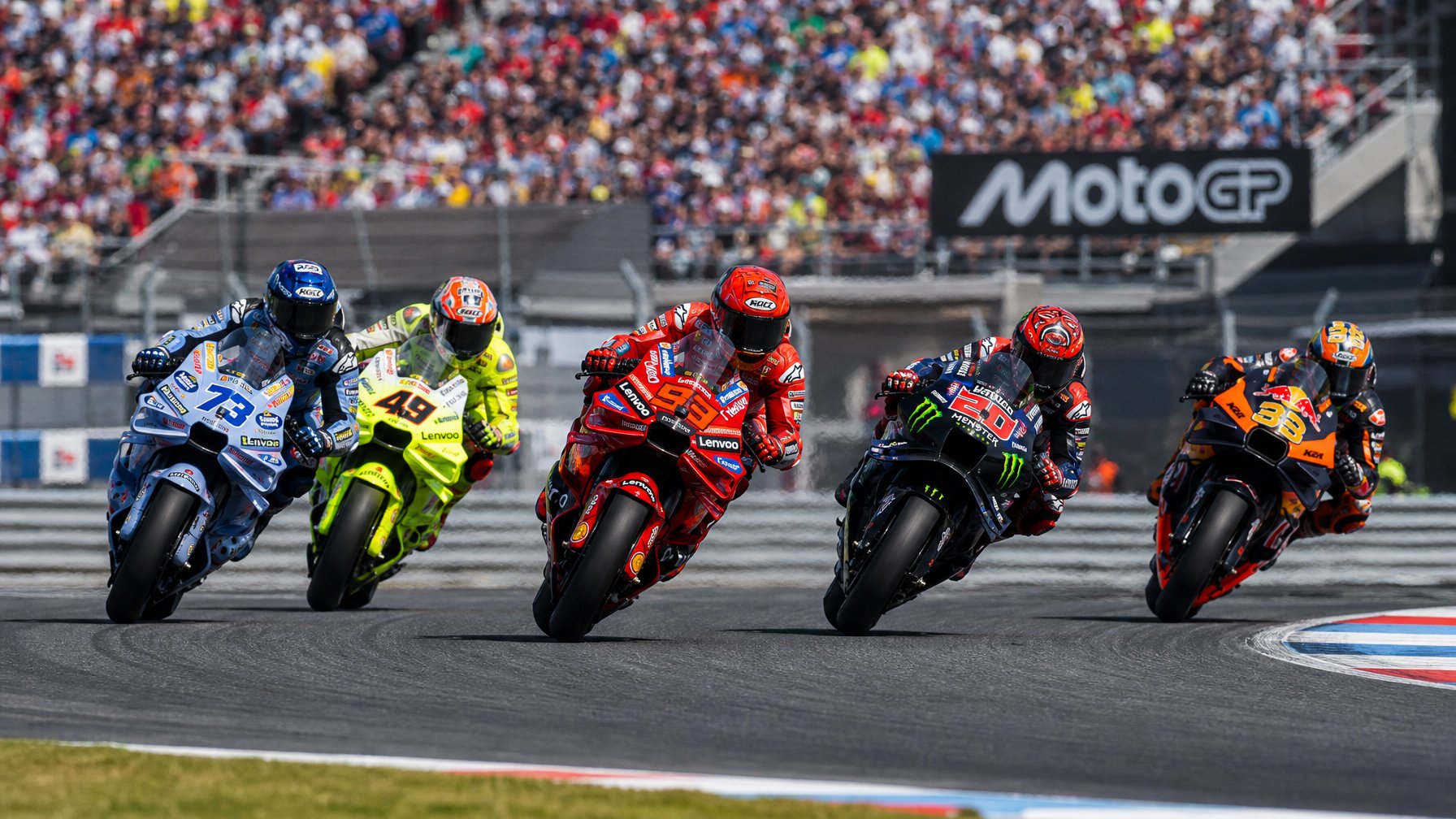 Lima pembalap MotoGP sedang balapan ketat di lintasan dengan penonton di latar belakang.
