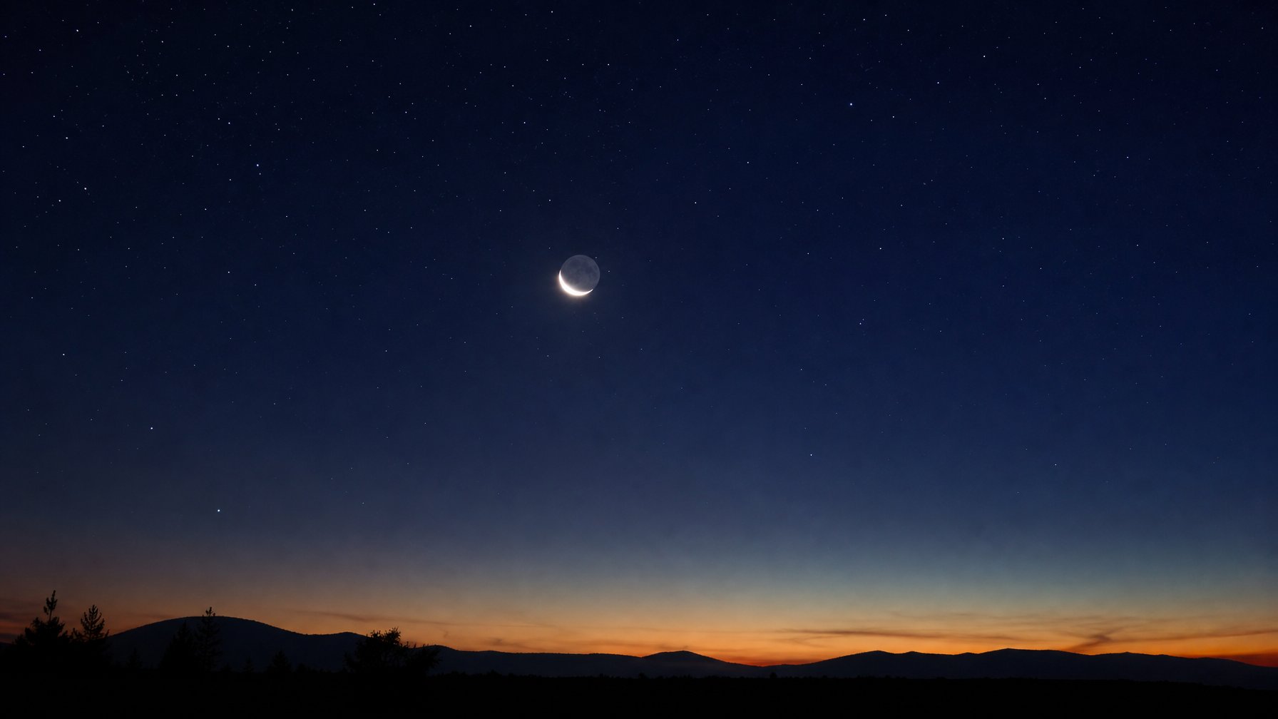 Langit malam yang gelap dengan planet Venus berbentuk sabit terang terlihat jelas di antara bintang-bintang, di atas siluet lanskap yang tenang.