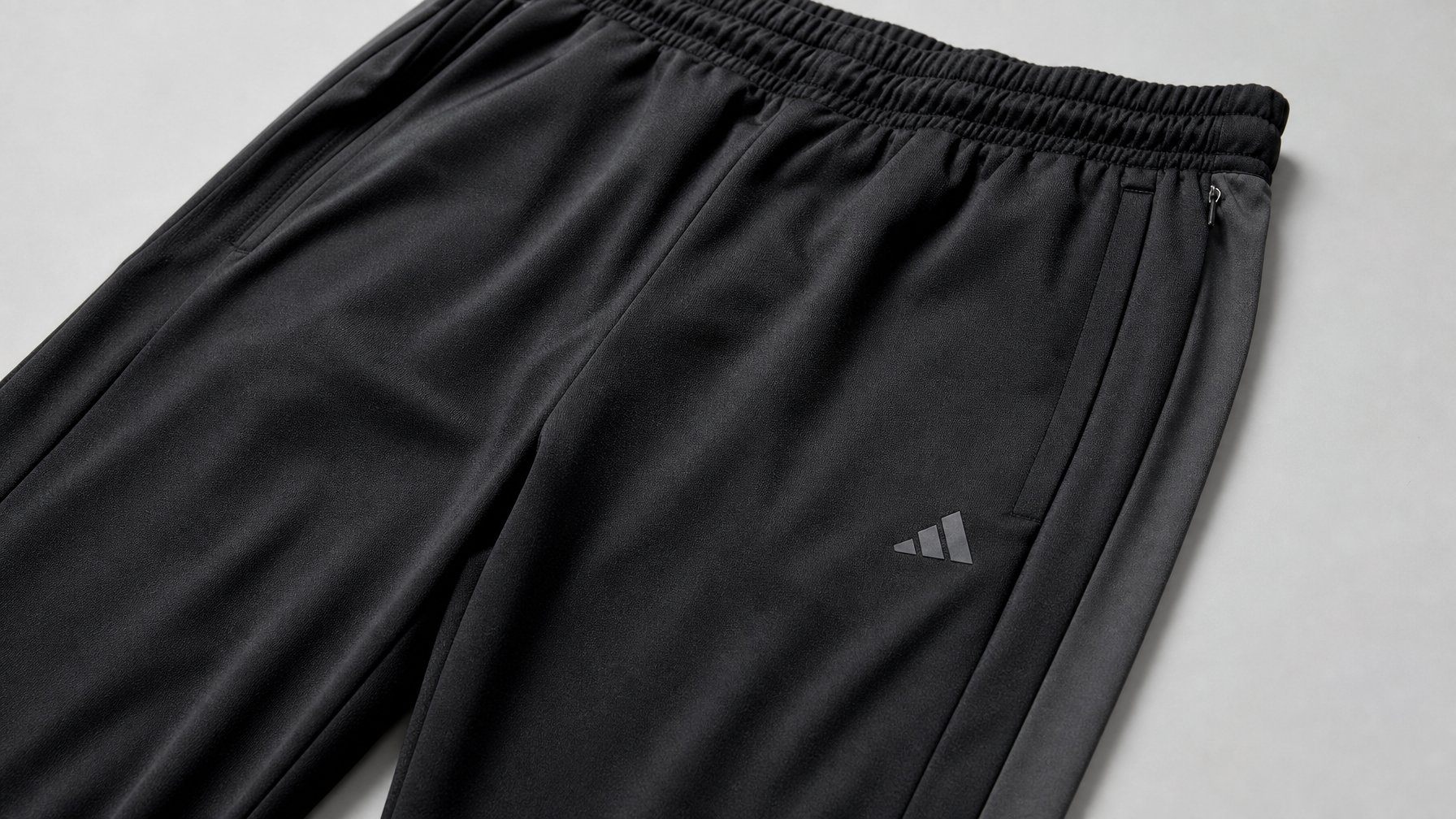 Sepasang celana training Adidas pria dengan bahan ringan dan tahan lama ditampilkan di latar belakang bersih.
